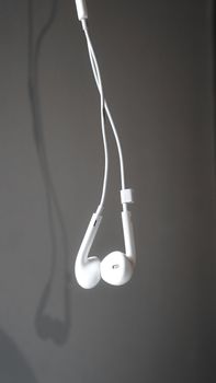 Close-up of white earphones hanging against a grey background with shadow details.