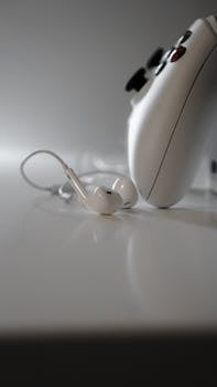 Close-up of white wireless earbuds and a gaming controller on a white surface.