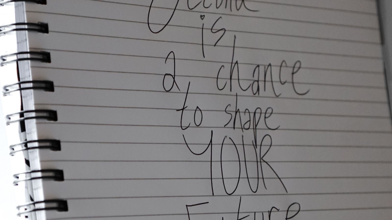 An open spiral notebook displaying a handwritten motivational quote