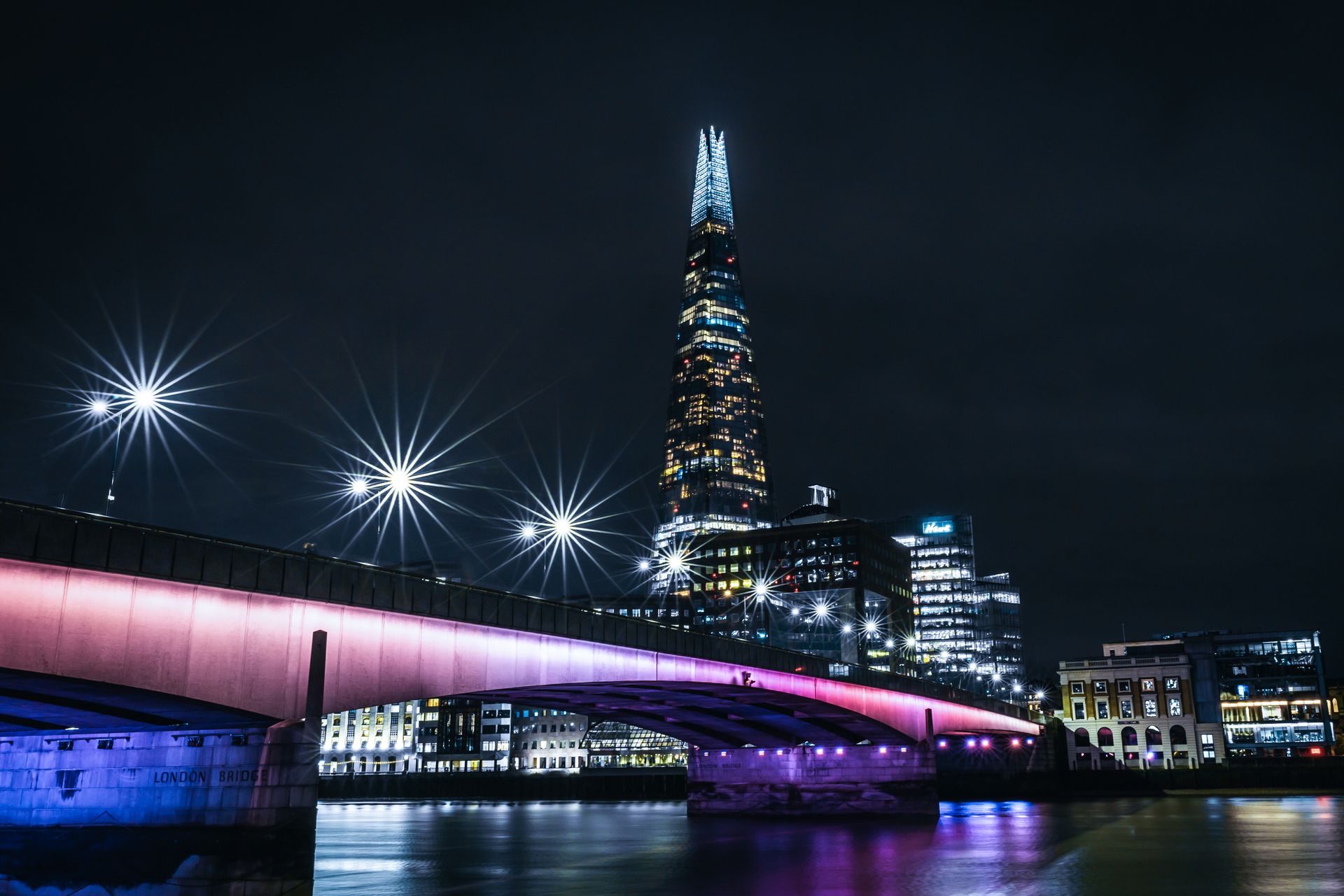 Stunning night cityscape featuring The Shard and colorful lights of London Bridge reflecting on the Thames.