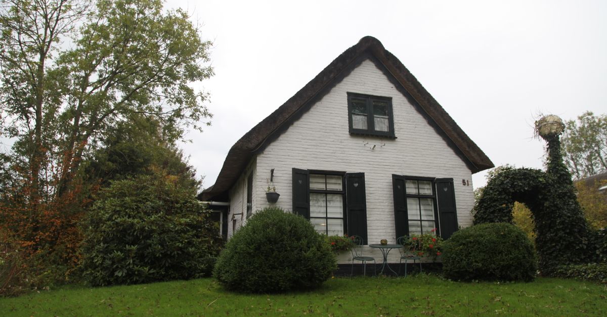 A quaint white cottage with a thatched roof surrounded by lush greenery and a well-kept garden.