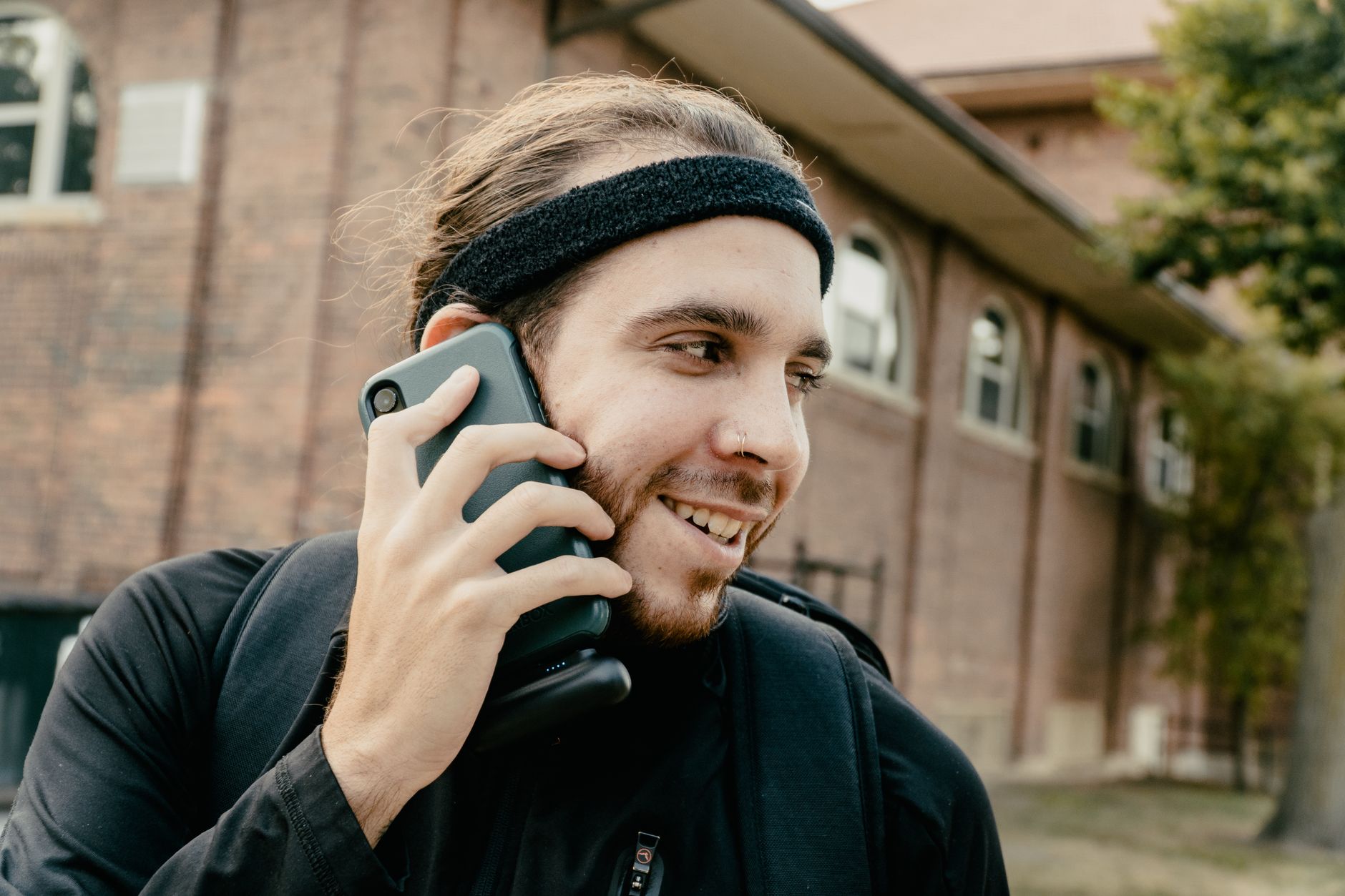 Young adult wearing a headband talking on a smartphone outdoors. Casual and happy expression.