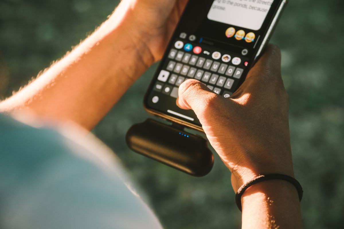 Hand typt op een smartphone terwijl een kleine powerbank onderaan de telefoon is aangesloten