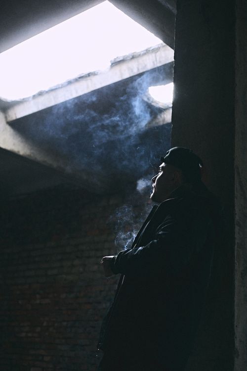 Free Man smoking in dimly lit urban setting, enveloped in smoke, depicting contemplation. Stock Photo