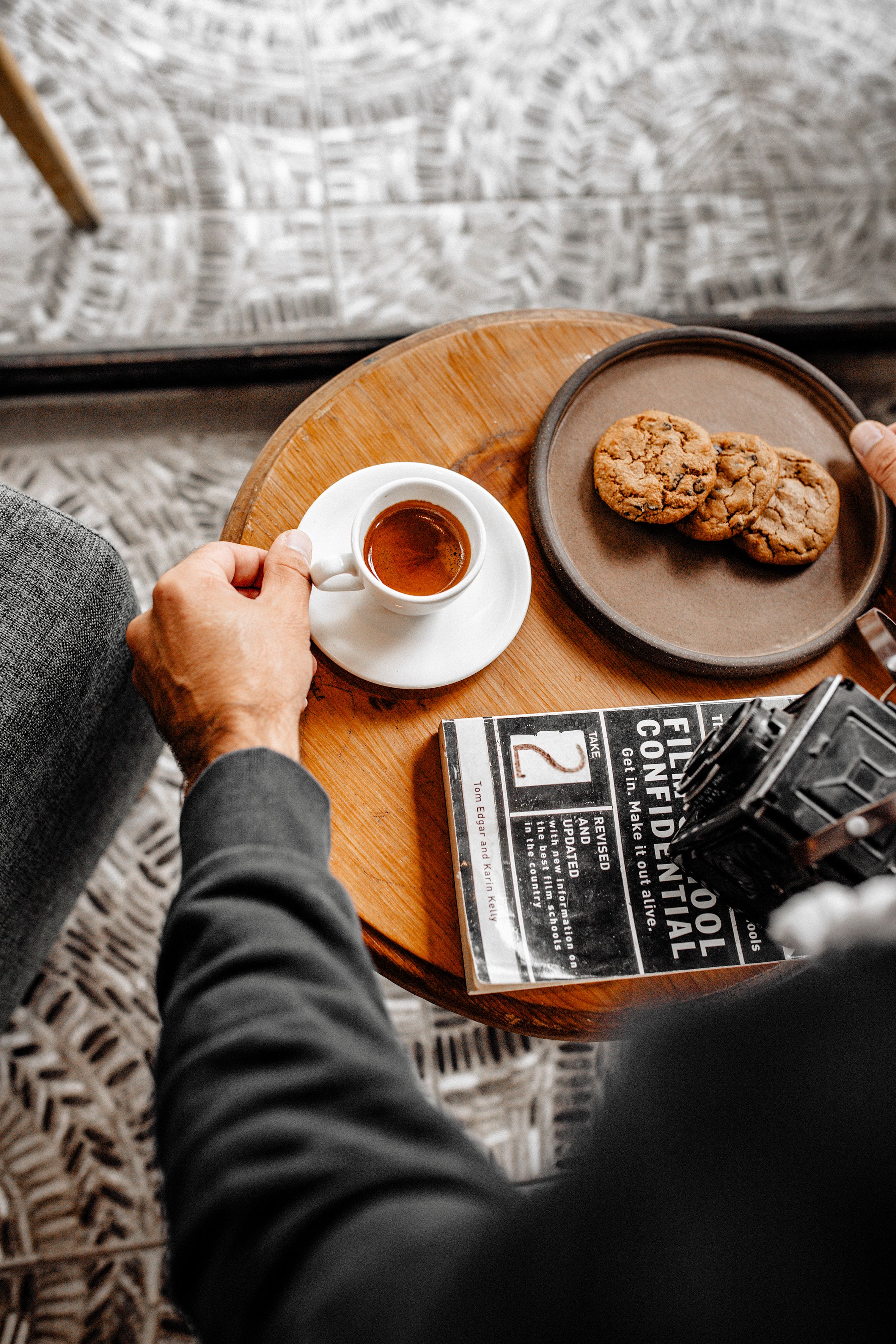 A stack of golden almond biscotti leaning against a small espresso cup, with crumbs and sliced almonds scattered on a wooden board.