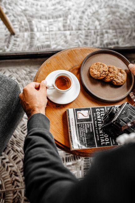 A stack of golden almond biscotti leaning against a small espresso cup, with crumbs and sliced almonds scattered on a wooden board.
