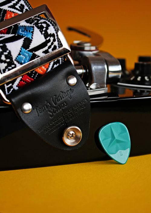 Free Detailed close-up of a guitar's strap and pick on a vibrant surface, emphasizing musical equipment. Stock Photo