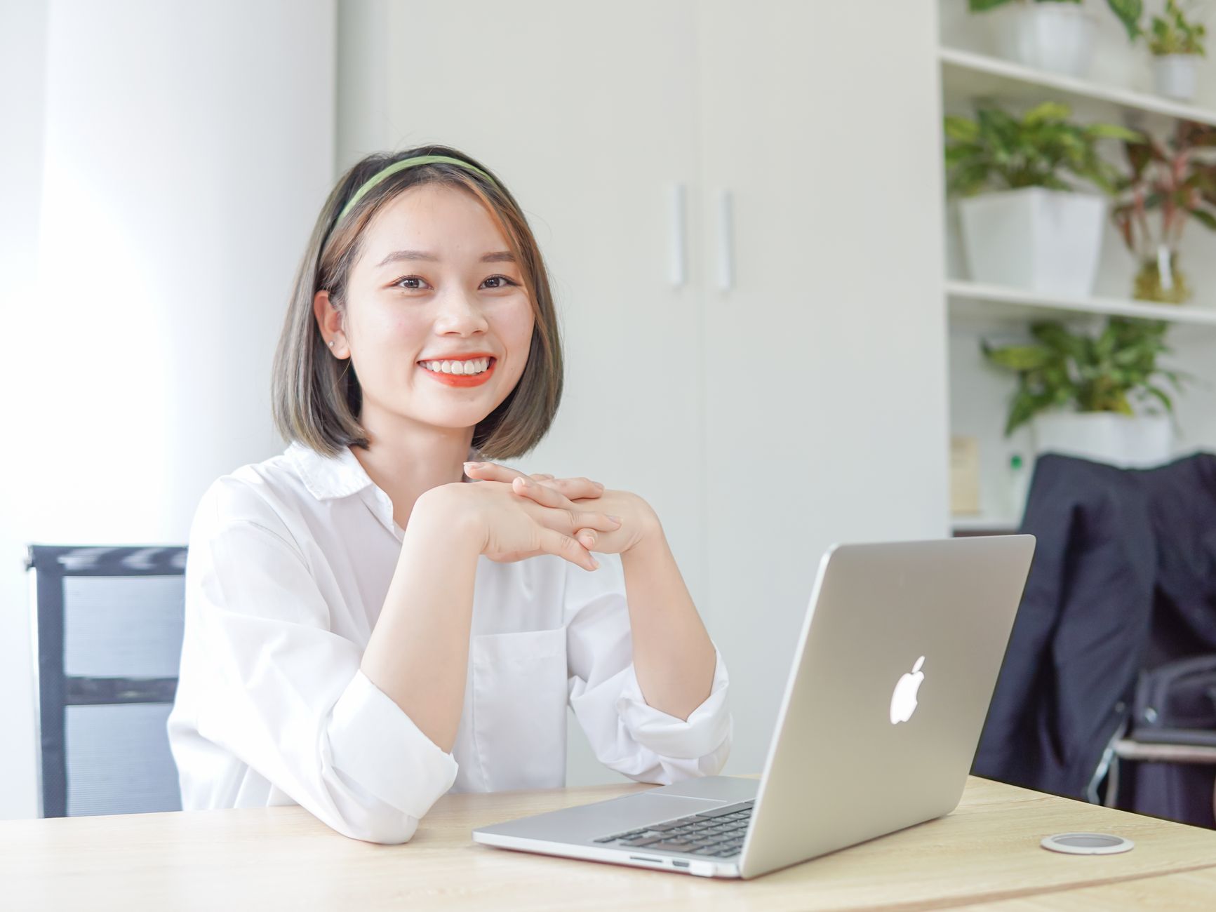 Woman sitting at desk with laptop, smiling confidently in a modern bright office setting.