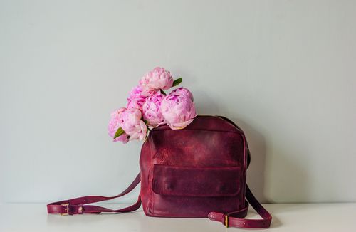 Free A stylish vintage leather bag adorned with pink peonies presenting a chic floral arrangement. Stock Photo