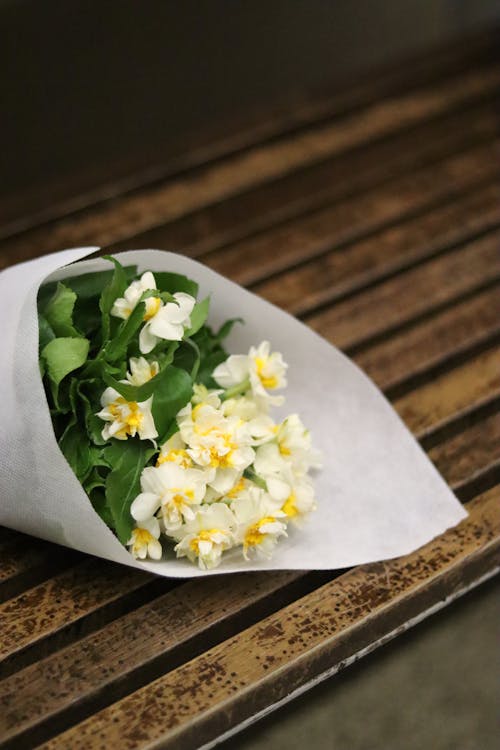 White Flowers Wrapped in Paper Laying on Bench 