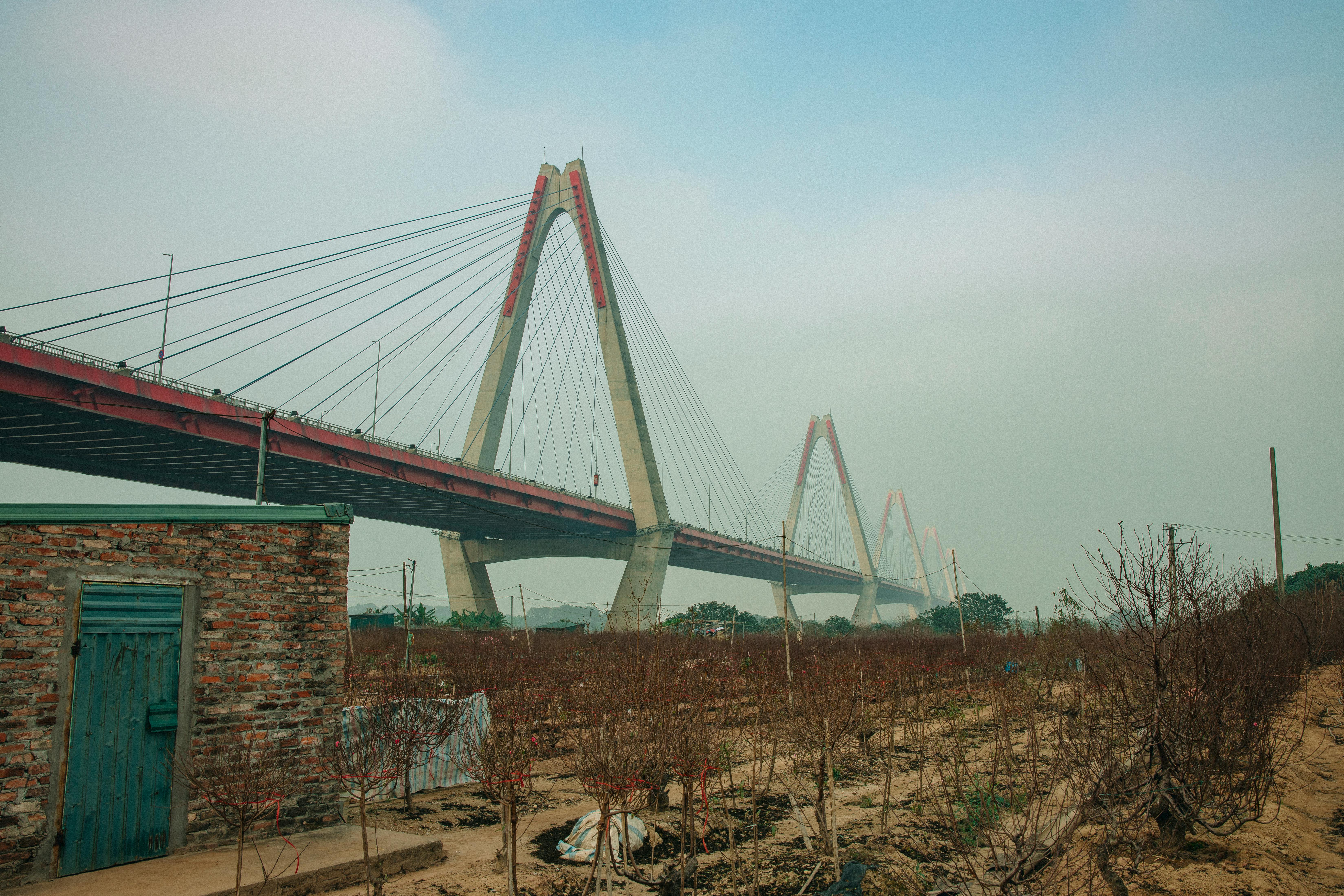 Suspension bridge in Vietnam extending over a rural landscape under a cloudy sky.