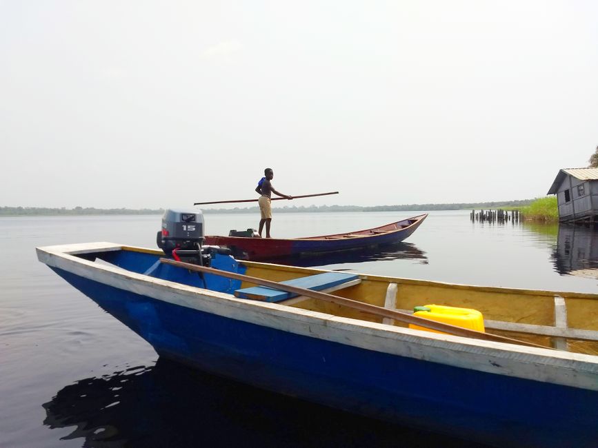A man stands on a wooden boat in a calm lake setting, showcasing aquatic transportation and tranquility.