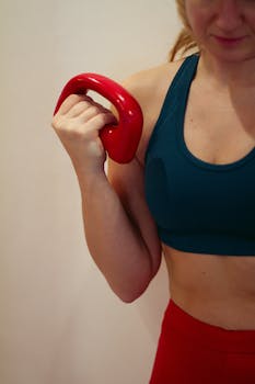 Close-up of a woman lifting a red kettlebell while working out indoors.