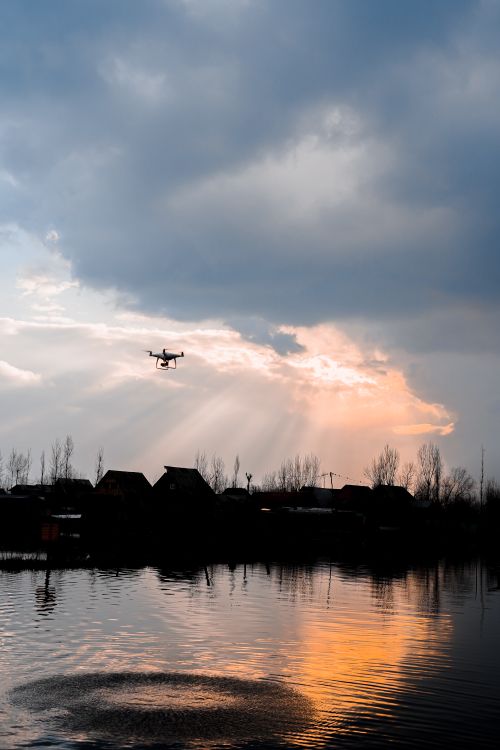 Free A drone flies over calm waters during a serene evening, reflecting a vibrant sunset sky. Stock Photo
