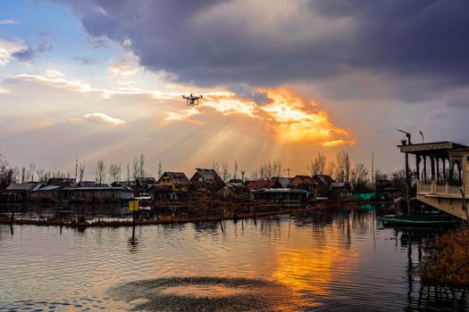 A scenic vertical shot of a drone flying over a riverside village during sunset, reflecting vibrant colors.