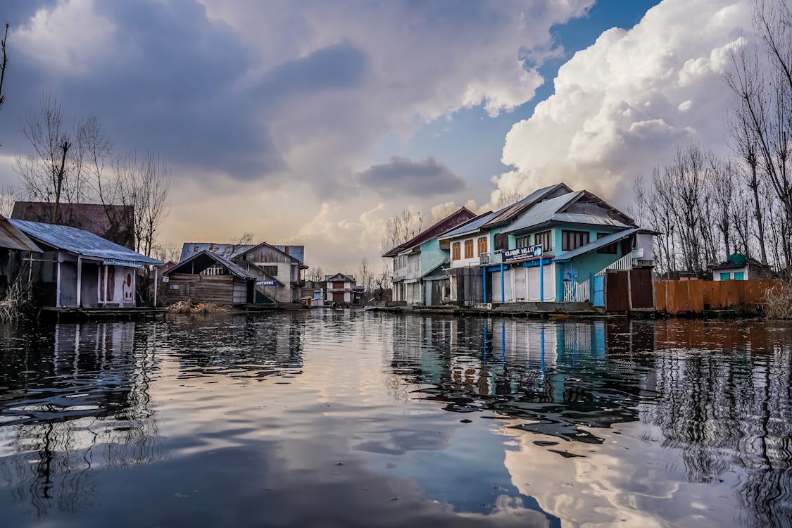 Free Blue and White Wooden Houses Beside River Under Blue and White Cloudy Sky Stock Photo