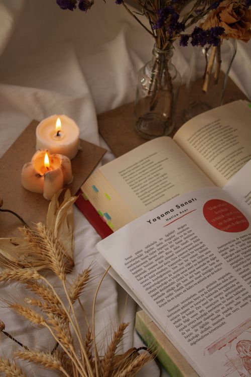 Free A warm, intimate setting with open books, lit candles, and dried flowers on a soft surface. Stock Photo