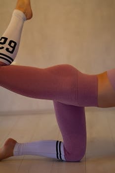 Close-up of a person in yoga pants performing a stretching exercise indoors.