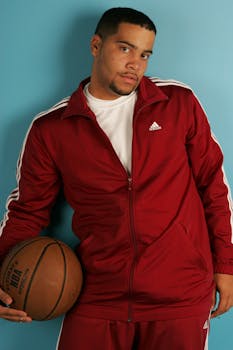 Man in red jacket posing with a basketball against a blue background.