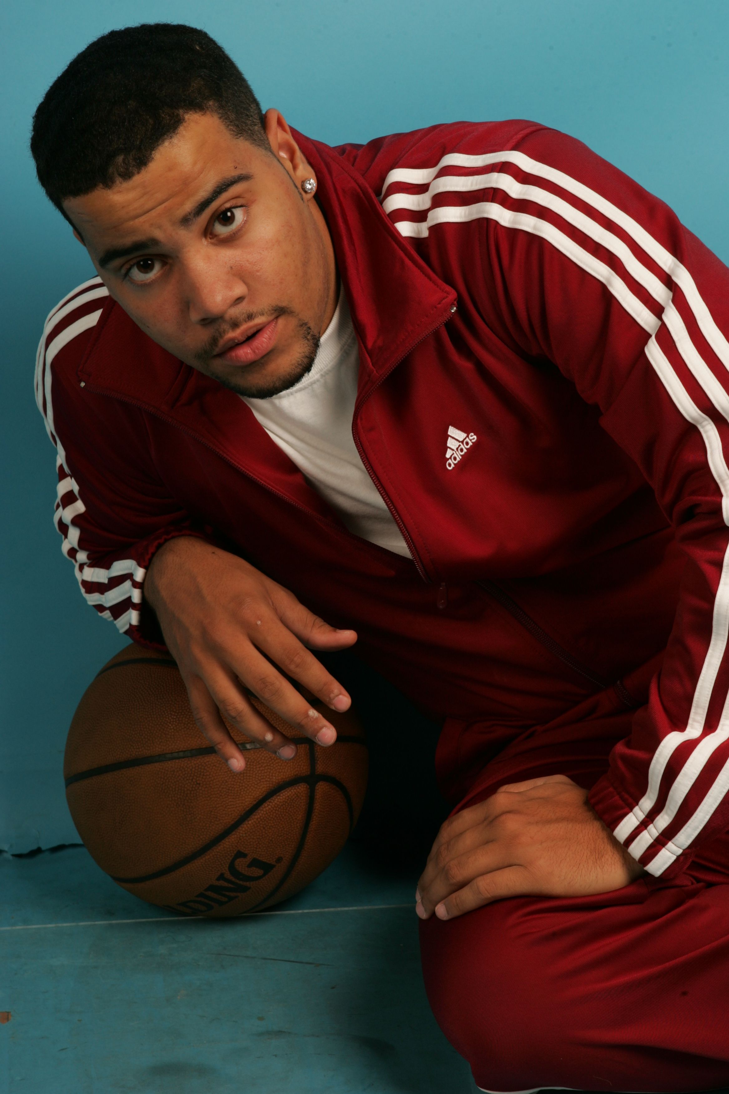 Portrait of a man in a red tracksuit holding a basketball, indoors.
