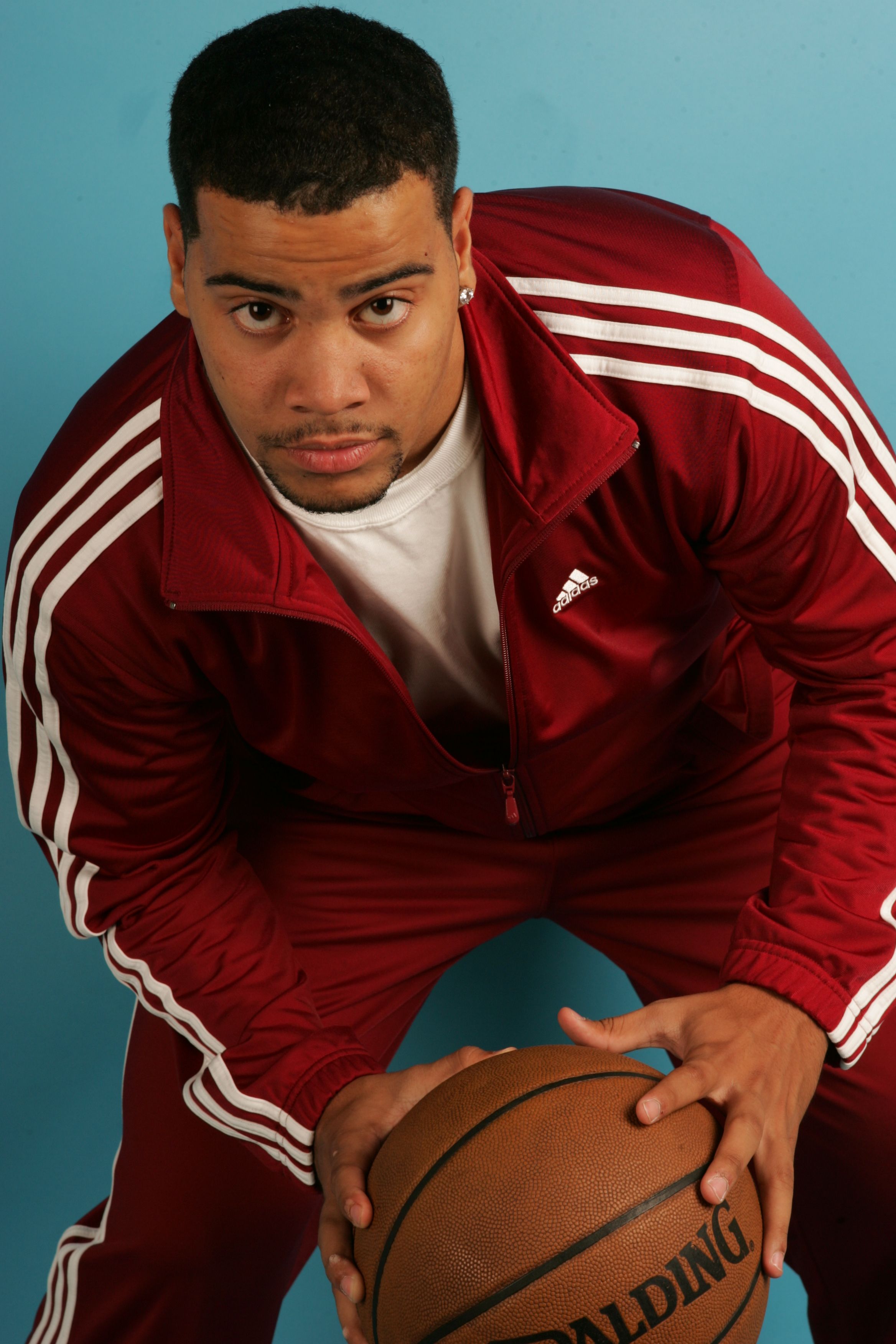 Focused portrait of a male basketball player holding a ball, wearing a red tracksuit.