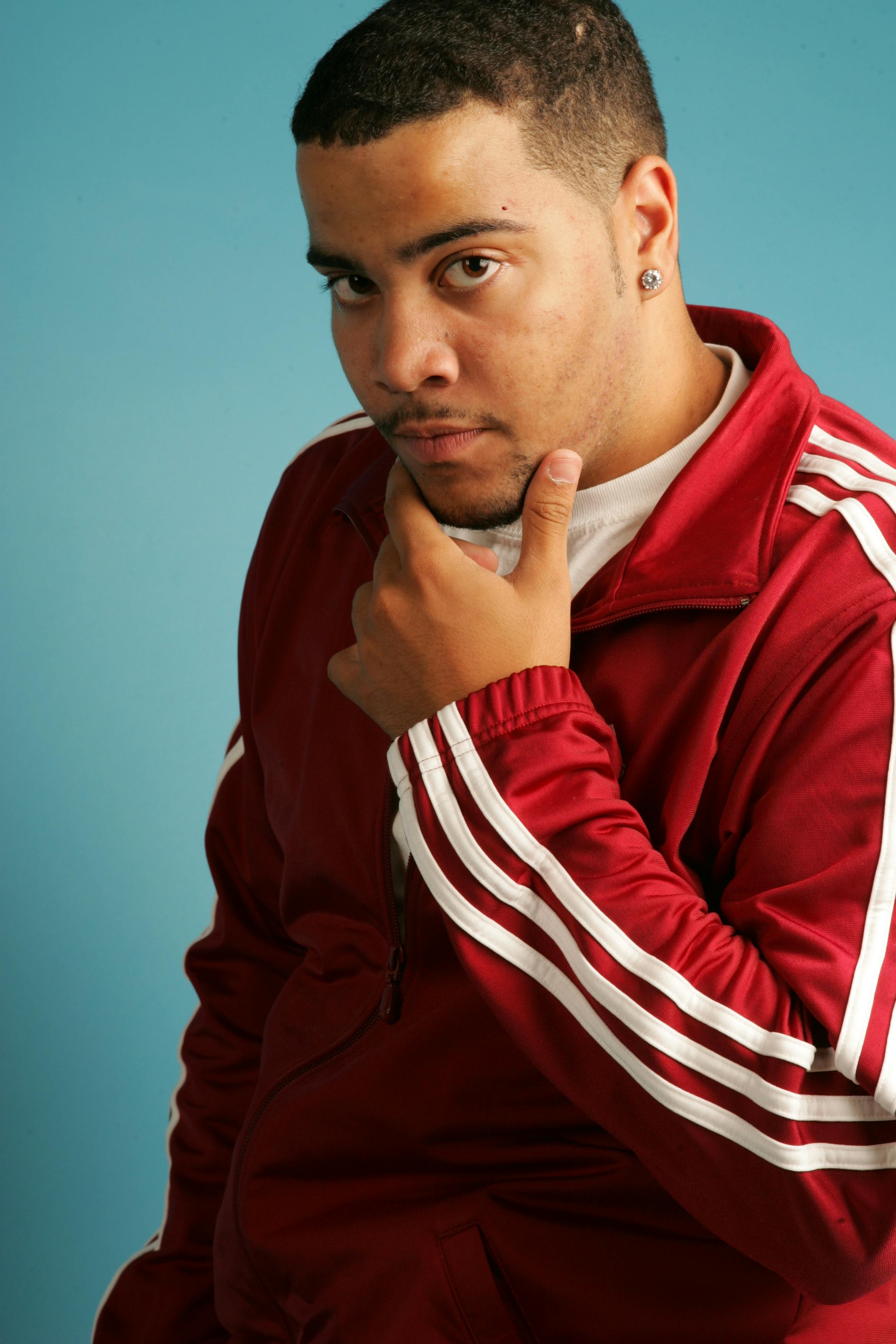 Man posing thoughtfully in a red jacket against blue background.