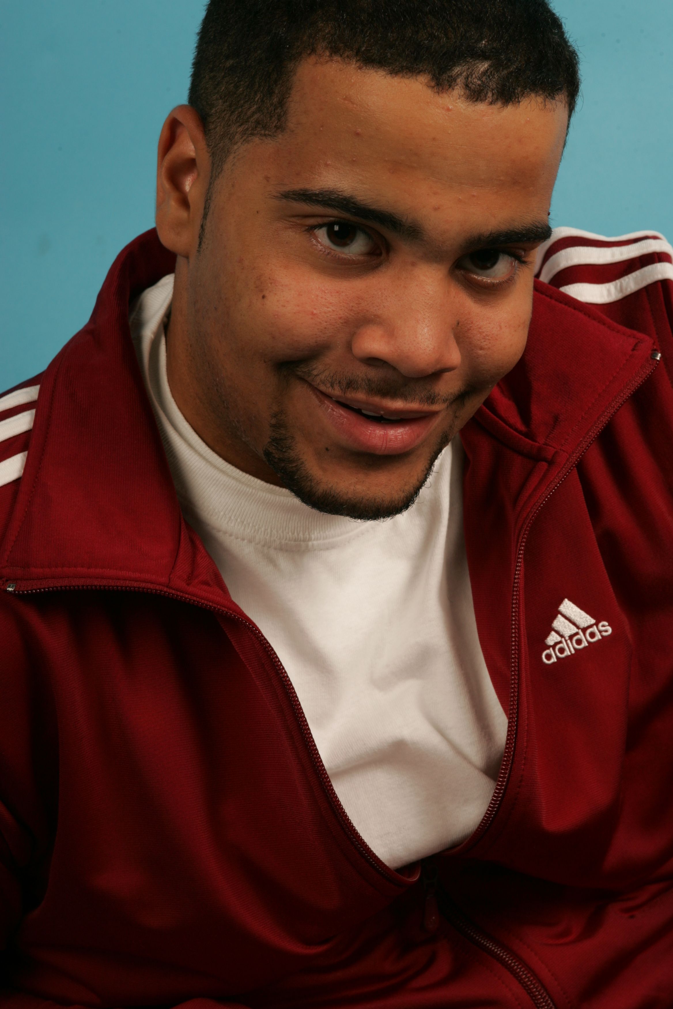 Portrait of a smiling man in a red jacket against a blue background, conveying warmth and positivity.
