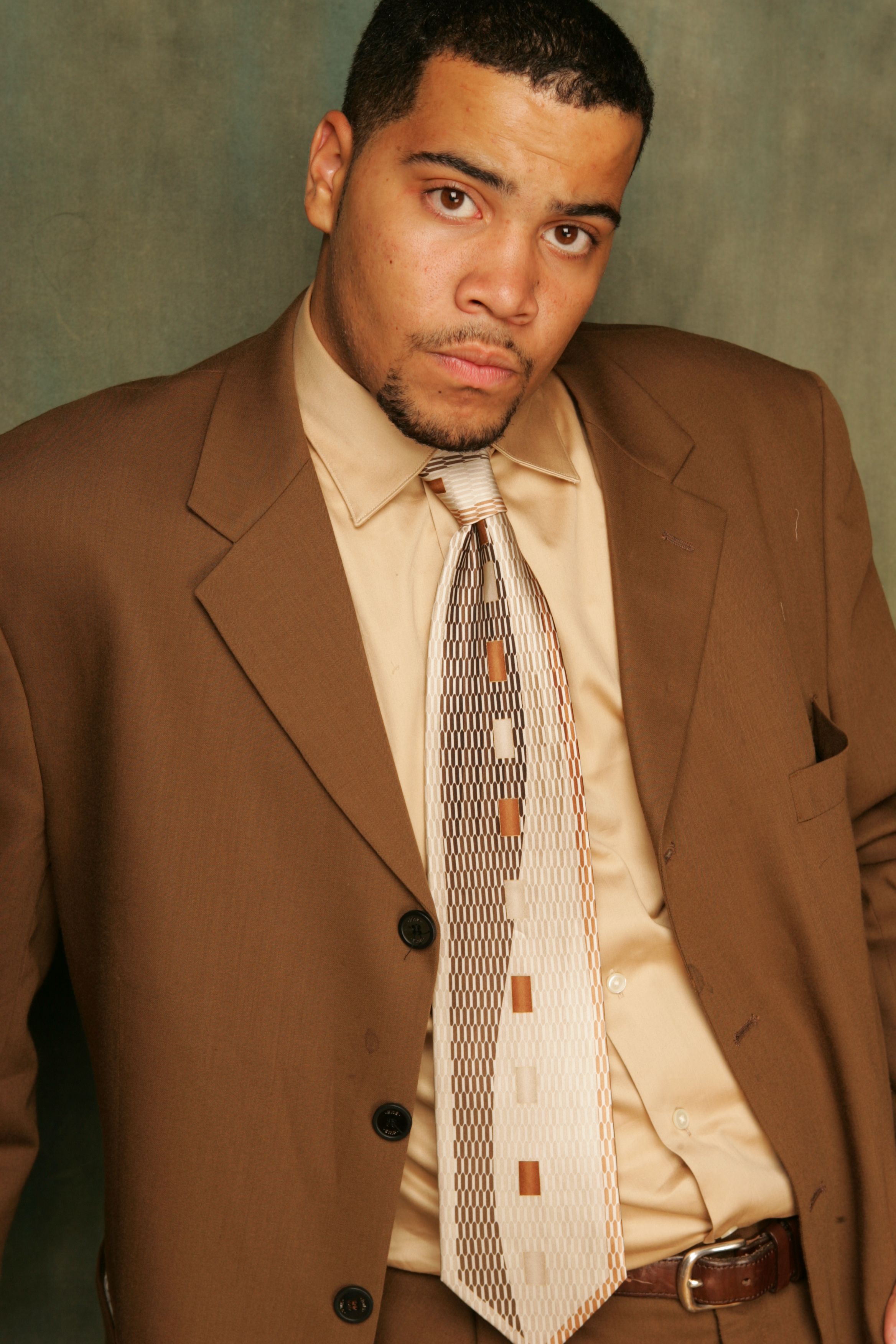 A confident man in a brown suit poses for a portrait, showcasing elegance and style.