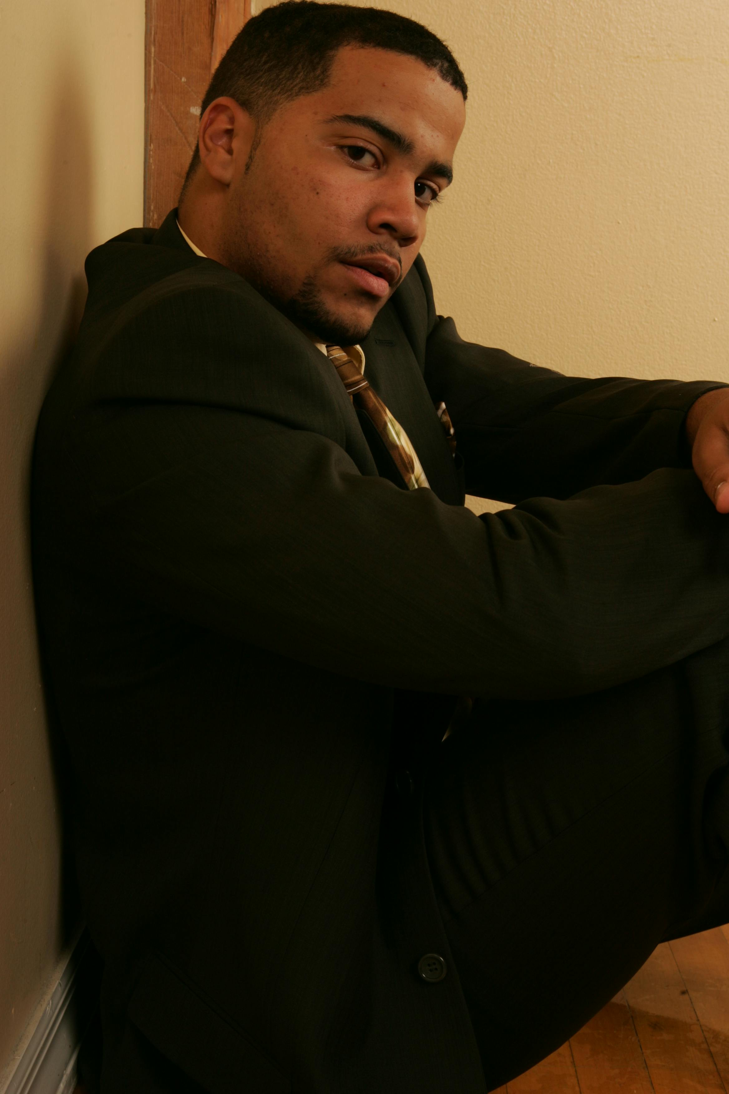 Confident man in a suit sitting against a wall inside, exuding elegance and style.