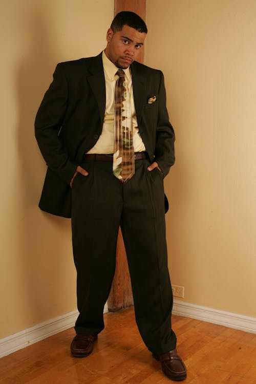 Man in Black Suit Standing Beside White Wall