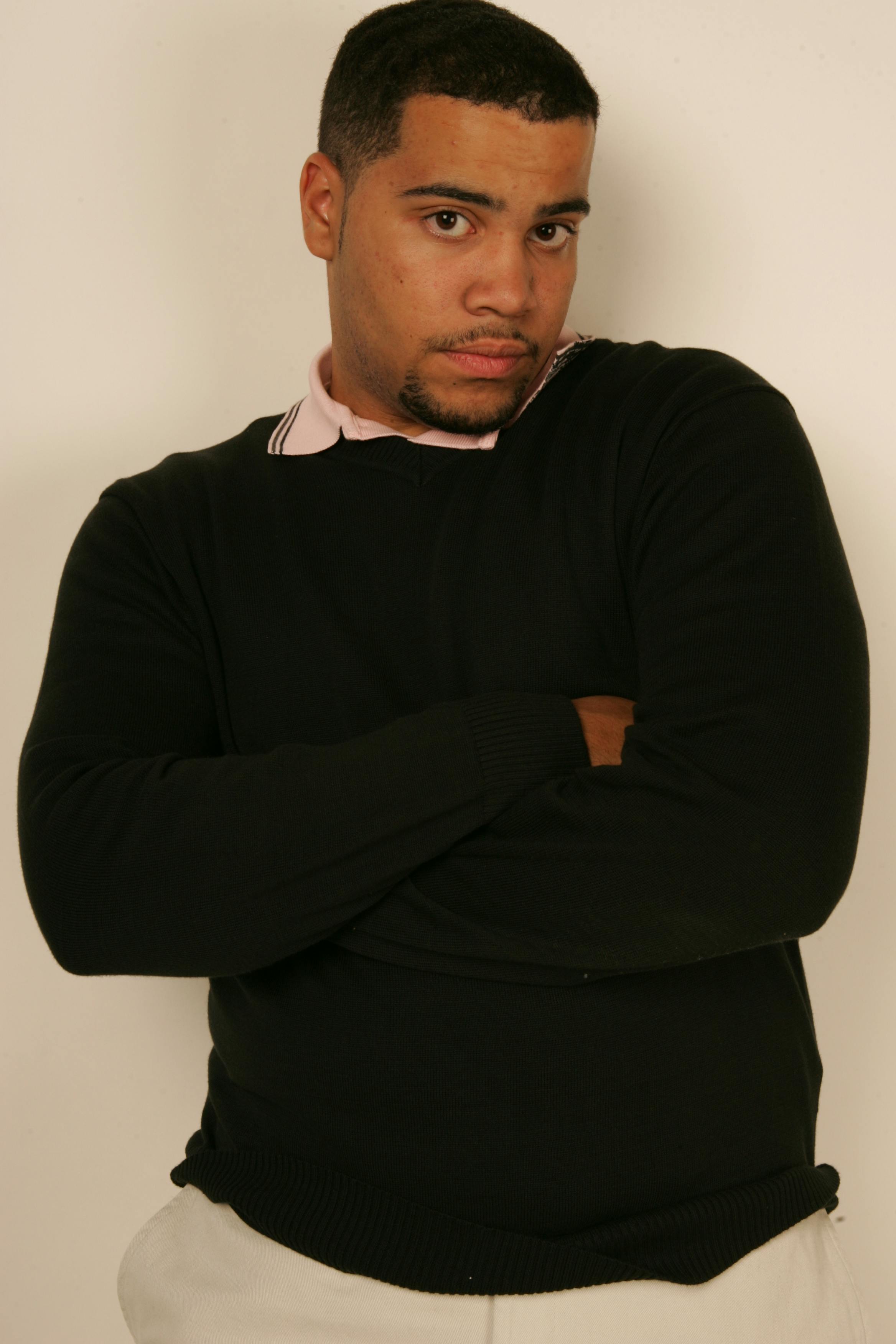 Confident man in a black sweater crossing arms, indoor portrait with neutral background.