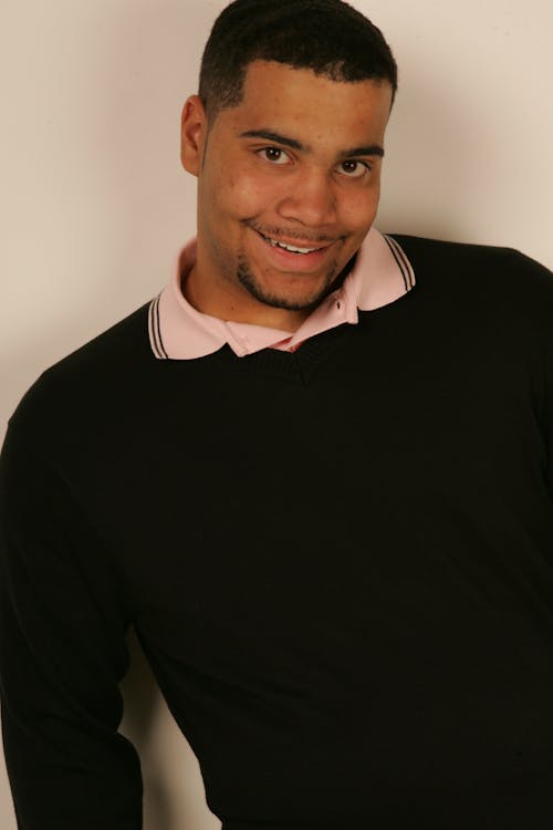 Man in Black Sweater Leaning on the Wall while Smiling at the Camera