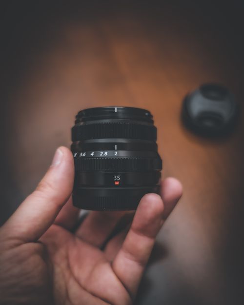 Free A close-up shot of a camera lens being held in a person's hand on a wooden surface. Stock Photo