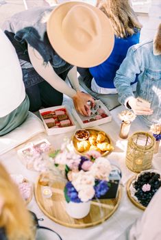Group of friends enjoying a sunny outdoor picnic with flowers, snacks, and drinks.