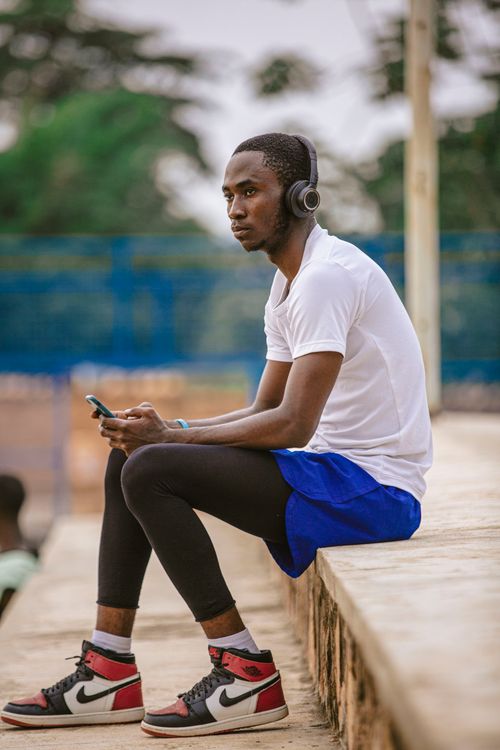 Free Man in sportswear sitting outdoors with headphones, enjoying music on a sunny day. Stock Photo