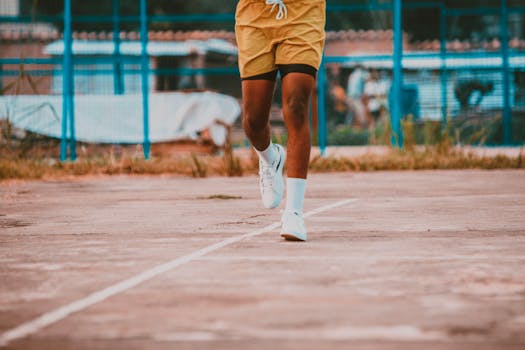 Close-up of a man's legs running on an outdoor basketball court, wearing yellow shorts and sneakers.