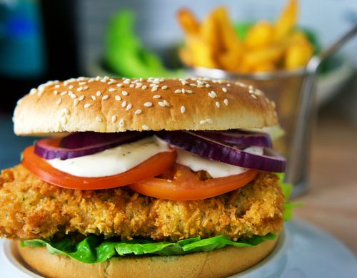 Free Delicious crispy chicken burger topped with fresh lettuce, tomato, onion, and a creamy sauce. Stock Photo