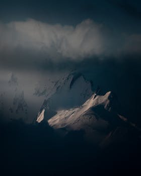 Dramatic view of snow-covered peaks surrounded by fog and clouds, perfect for a moody landscape.