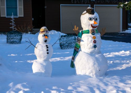 Free Two playful snowmen with scarves and hats in a snowy yard. Stock Photo