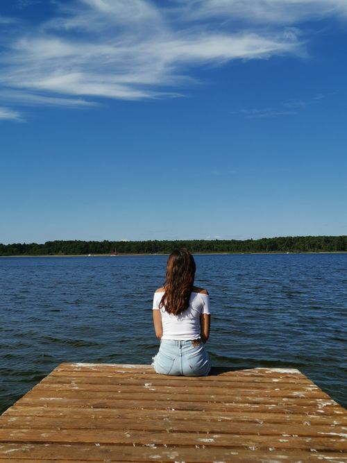 Free A woman sits on a dock in Sanguinet, France, gazing at the calm lake under a clear sky. Stock Photo