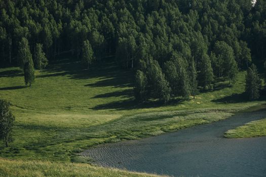 Explore a tranquil lakeside surrounded by lush green forests and rolling grasslands.