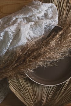 Artistic composition featuring pampas grass, lace, and a ceramic plate for elegant interior decor.