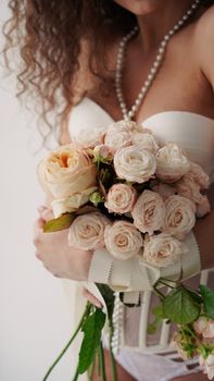 A woman with curly hair holding a delicate bouquet of roses, wearing a corset and pearl necklace.