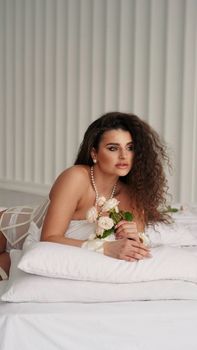 An elegant woman with curly hair holding flowers in a modern, minimalist indoor setting.