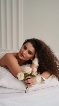 A serene portrait of a woman with curly hair and white roses, against a light backdrop.