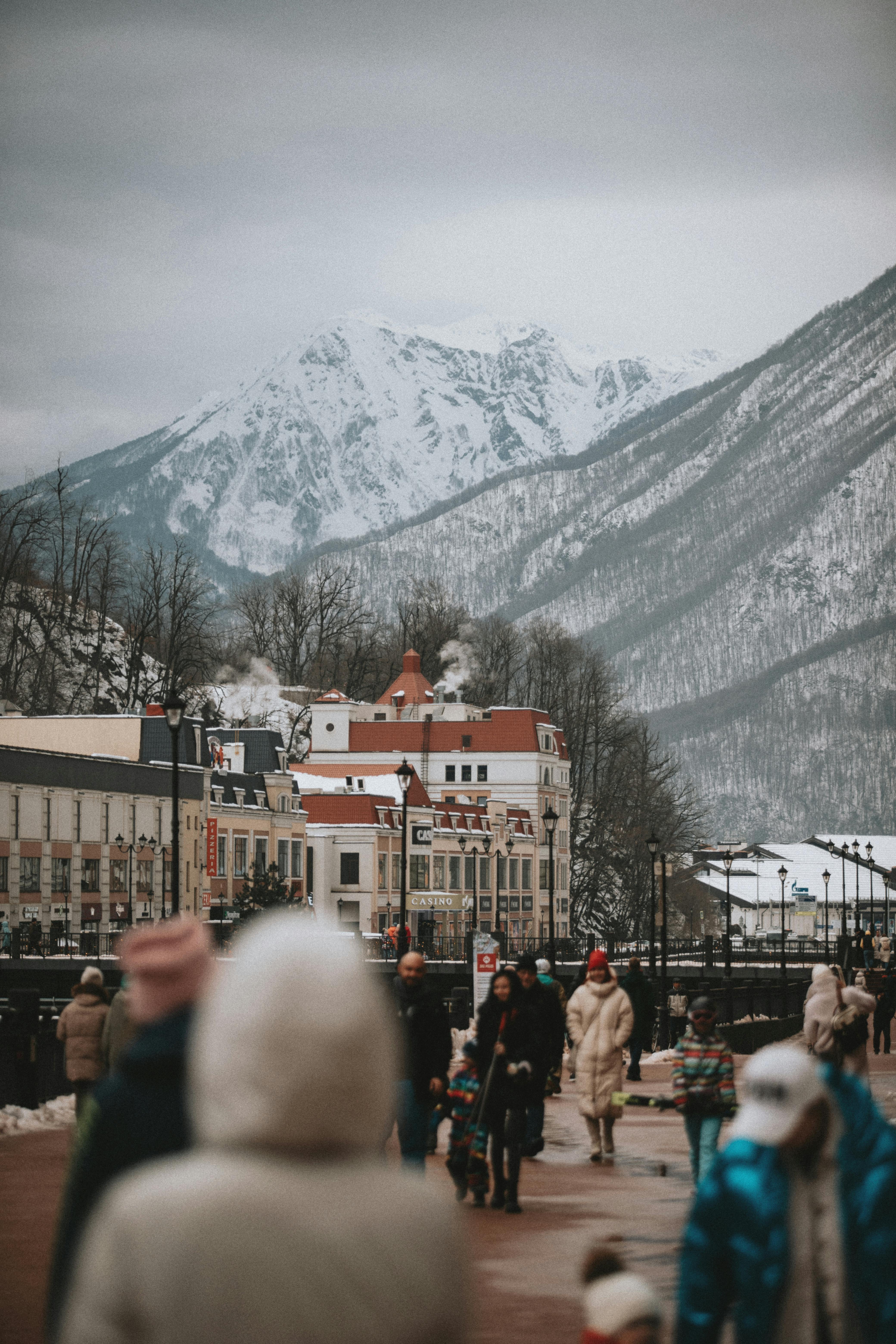 people walking on the street near buildings and snow covered mountain