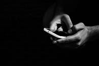 一张黑白照片，背景是黑色，画面中有人手持智能手机