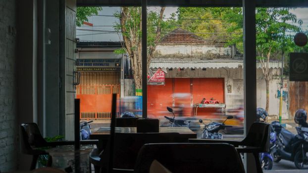 Blurred motorbikes pass by a street seen from inside a cafeteria in Pamekasan, Indonesia.