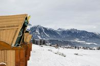 Scenic winter view of wicker chairs overlooking snowy mountains and village in Upper Austria.