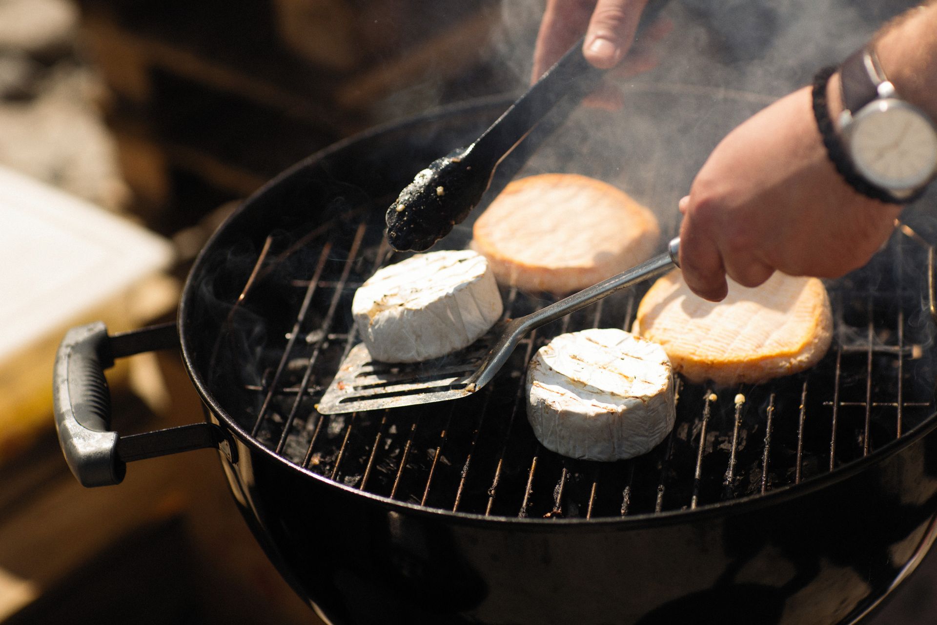 A close-up of Brie cheese and bread slices being grilled on an outdoor barbecue.